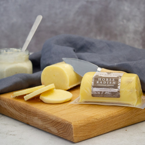 Lifestyle image of the Horseradish Infused Cheddar Cheese Barrel served on a cheeseboard